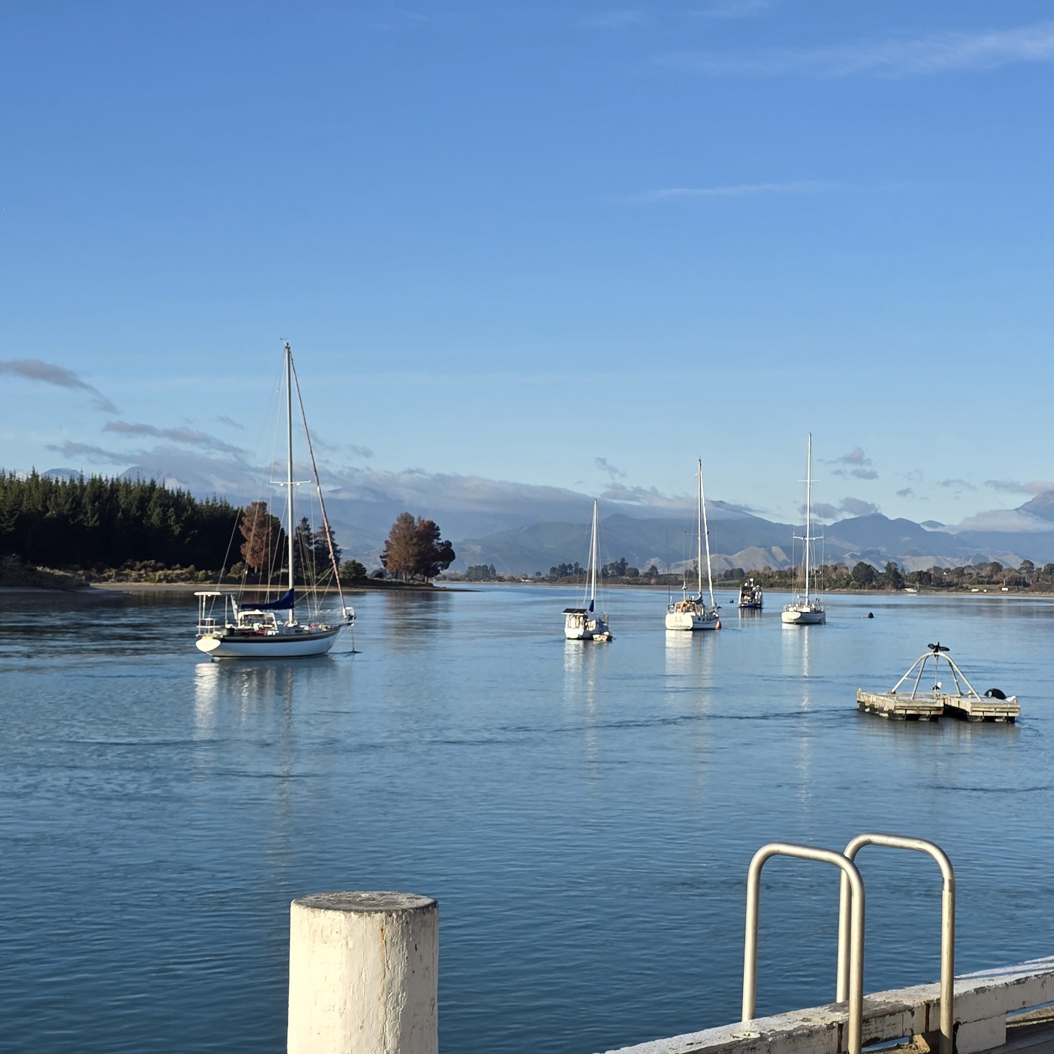 Yachts at anchor on a calm blue estuary with distant ranges beyond